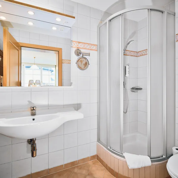 Modernes Hotelbad mit Glasdusche, weißem Waschbecken, Spiegel und gefliesten Wänden