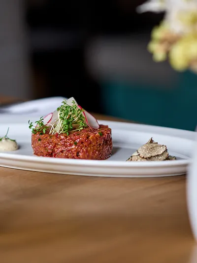 Beef tartare with radish, microgreens, truffle and mustard sauce on white plate with beer