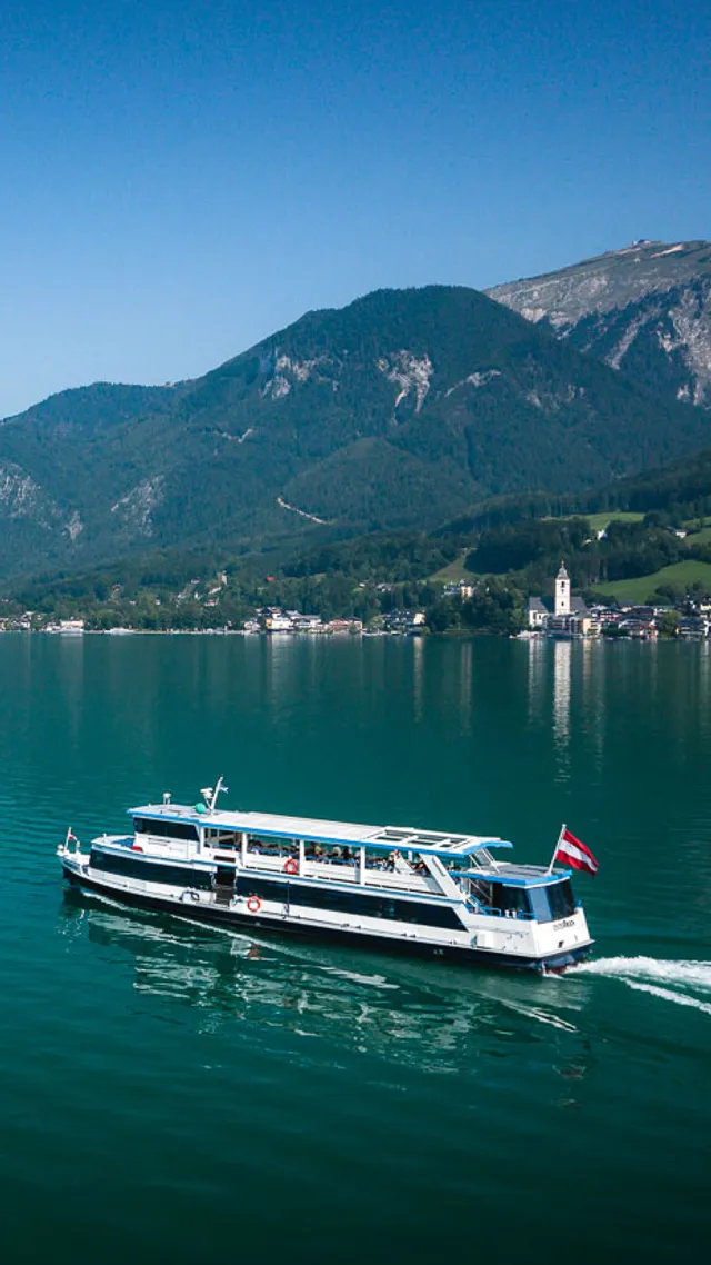 Passenger boat cruising on Lake Wolfgang with mountain village and Alps in background