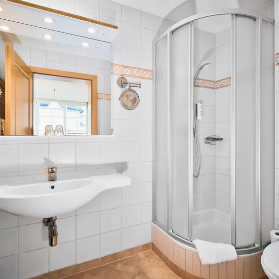 Modern hotel bathroom with glass shower, white sink, mirror and tiled walls