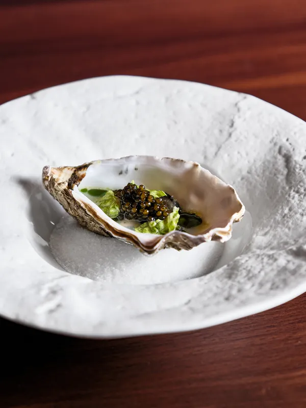 Gourmet oyster dish with caviar and greens served on white ceramic plate