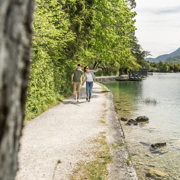 Couple walking along a lakeside trail surrounded by greenery in a mountain landscape