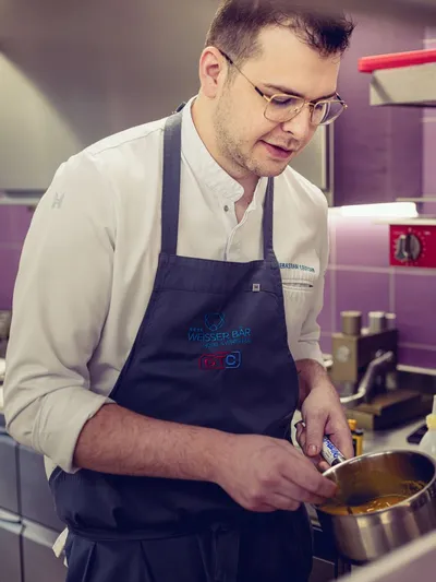 Chef in professional kitchen stirring sauce in stainless steel pot