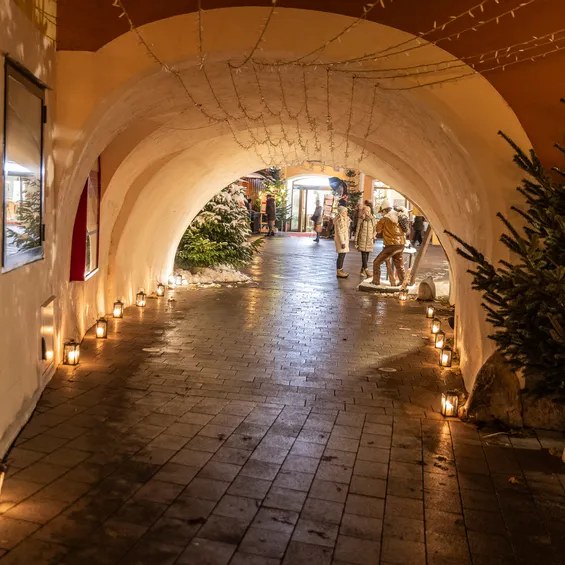 Festive archway with Christmas lights, candles, and decorated trees in a European town market