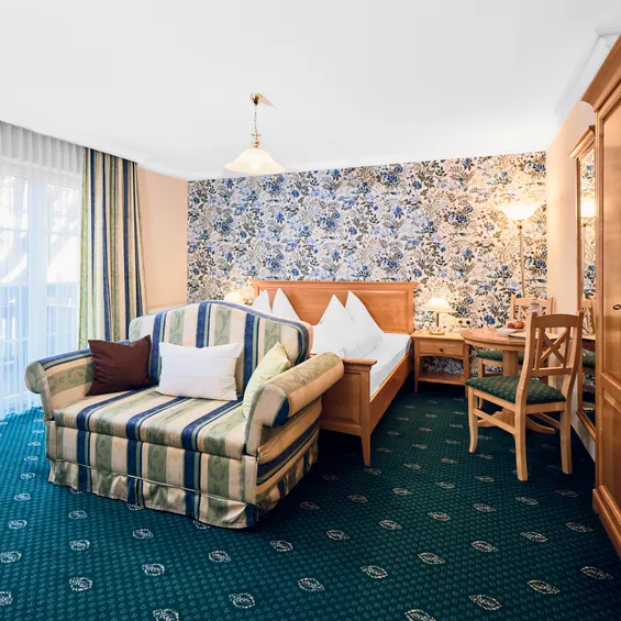 Cozy hotel room with floral wallpaper, striped sofa, double bed, and wooden furniture