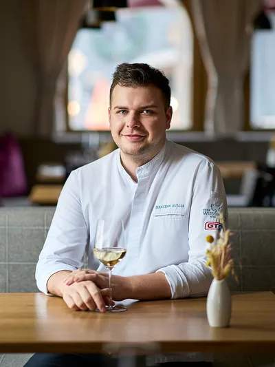Koch in weißer Uniform sitzt am Restauranttisch mit einem Glas Weißwein
