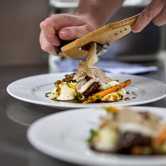 Koch hobelt frische Trüffel auf Gourmetgericht mit Fleisch, Kartoffelpüree und Karotten