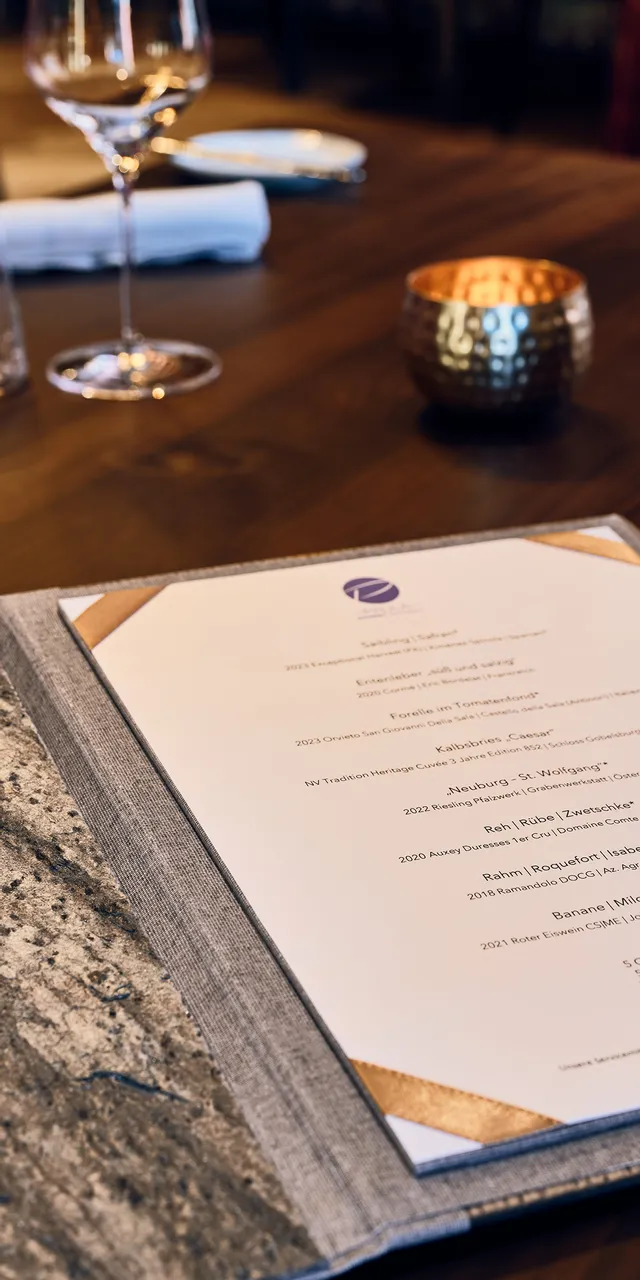 Elegant restaurant table setting with open menu, wine glasses, and candle on wooden table