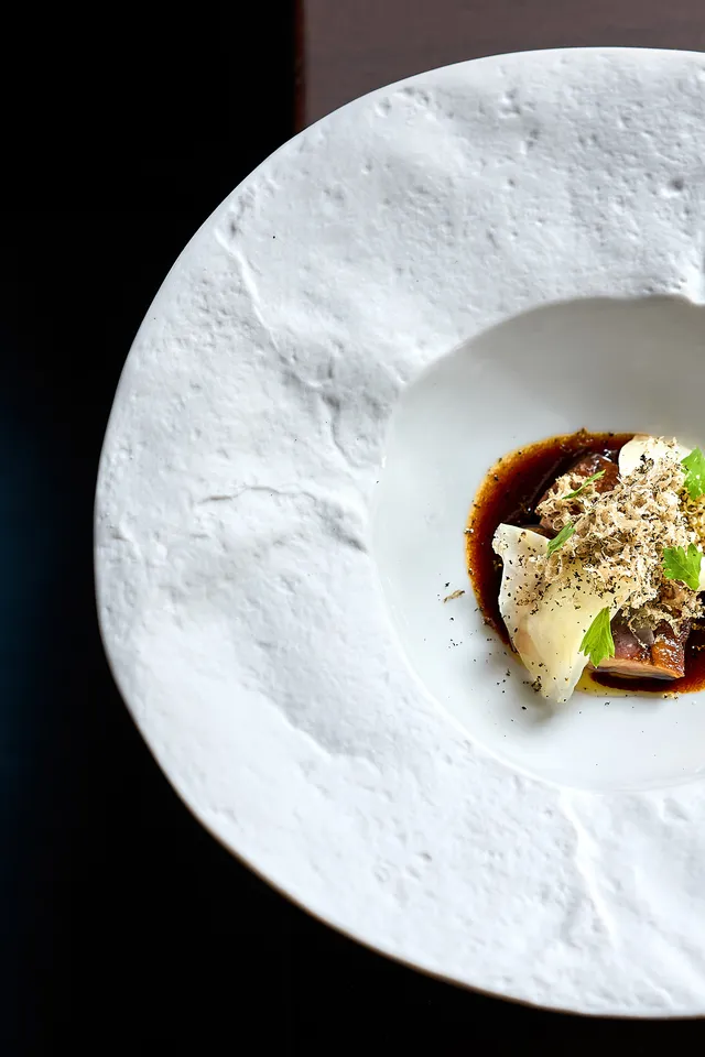 Gourmetgericht mit Trüffelspänen, Sauce und Garnitur auf strukturiertem weißen Teller