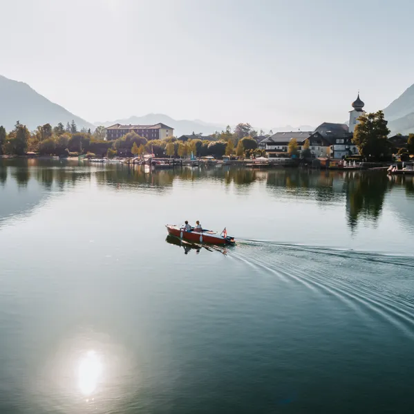 Couple in a small boat on clear alpine lake near picturesque Austrian village and mountains