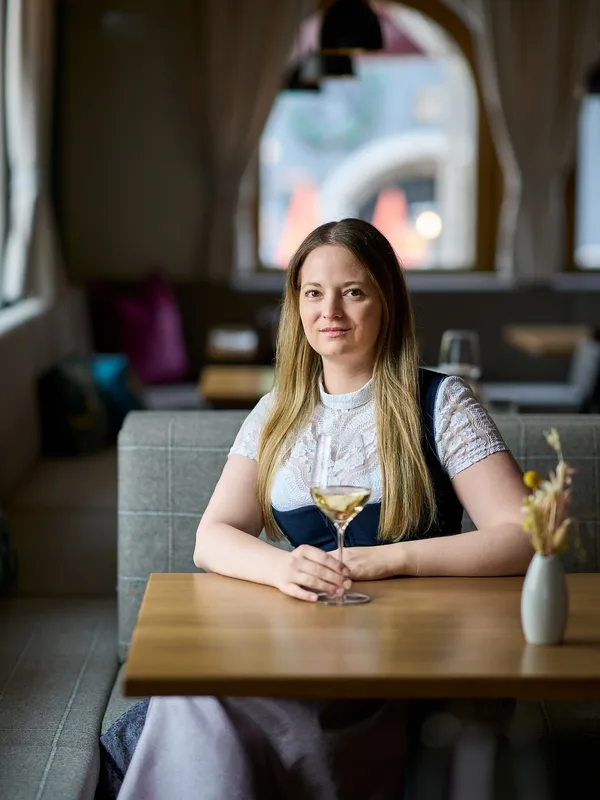 Woman with long blond hair holding a wine glass seated in a stylish restaurant interior