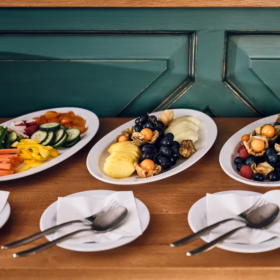 Plates with fresh cut vegetables and assorted fruits on a wooden counter