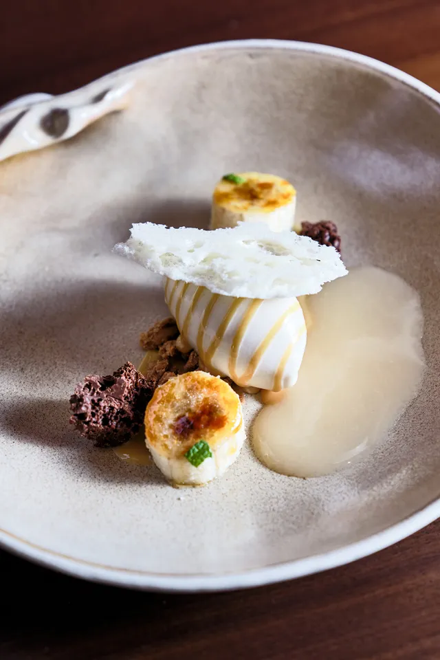 Gourmet-Dessert mit Eiscreme, Bananenscheiben, Schokoladencrumble und weißem Tuile angerichtet