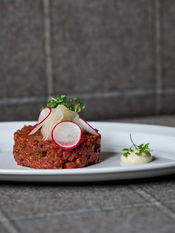Rindertatar mit Radieschenscheiben, Microgreens und Sauce auf weißem Teller