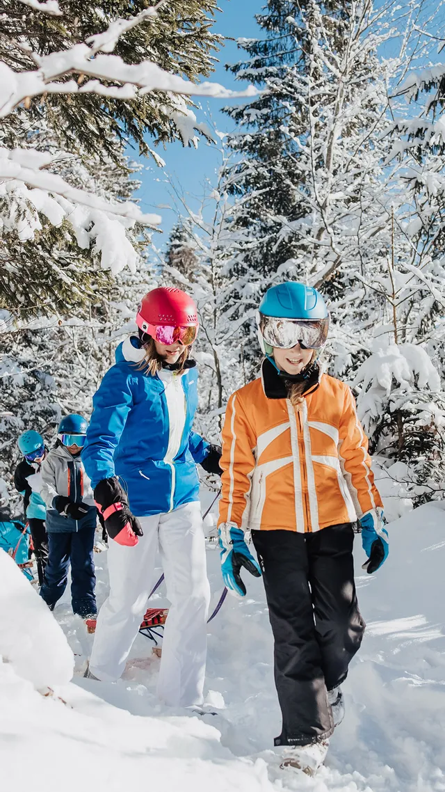 Children snowshoeing through snowy forest trail in bright winter gear
