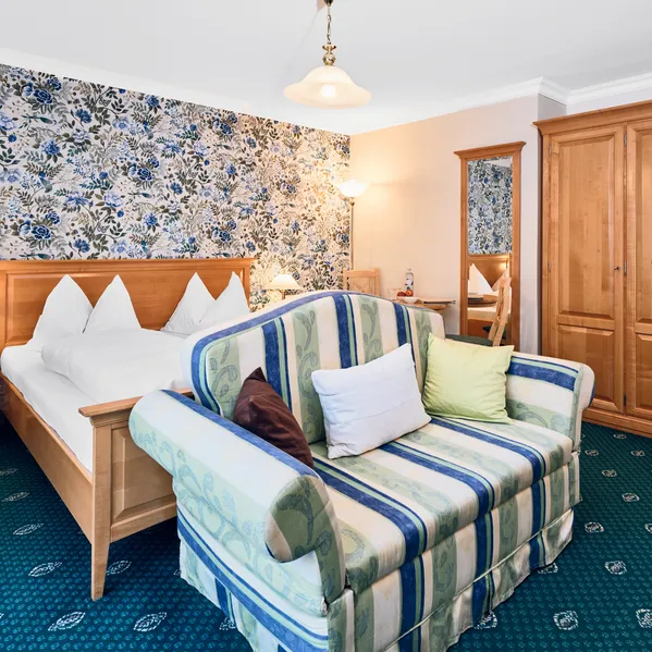 Cozy hotel room with floral wallpaper, wooden furniture, and striped loveseat