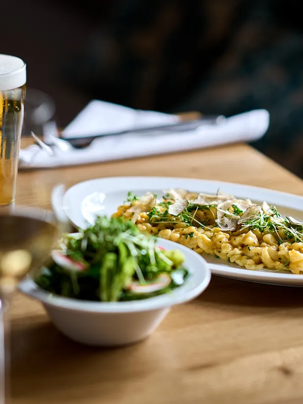Creamy truffle spaetzle with fresh salad and beer on a wooden restaurant table