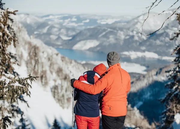 Couple in winter hiking gear admiring snowy alpine mountain landscape with lake view