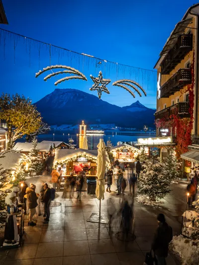 Festive Christmas market with lights and snow in a town square near mountains at dusk