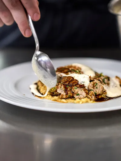 Koch richtet Kalbsmedaillons mit Schaumsauce auf einem weißen Teller an