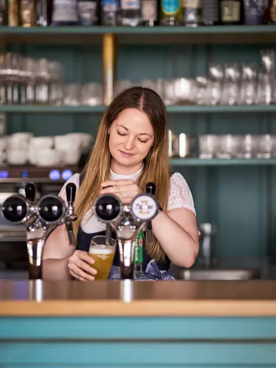 Bartender pouring draft beer behind bar with glassware and liquor bottles in background