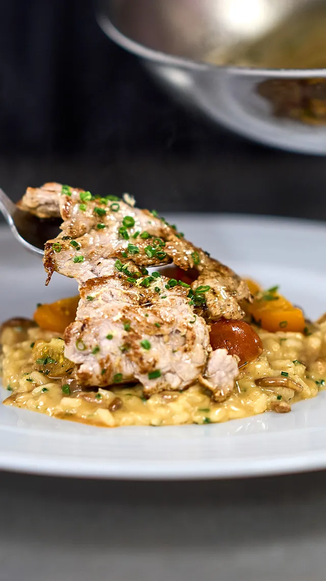 Cremiges Risotto mit gegrilltem Hähnchen und Gemüse wird in einer Profiküche angerichtet