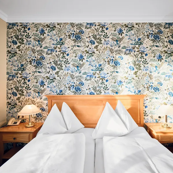 Cozy hotel room with floral wallpaper, twin pillows, and wooden headboard