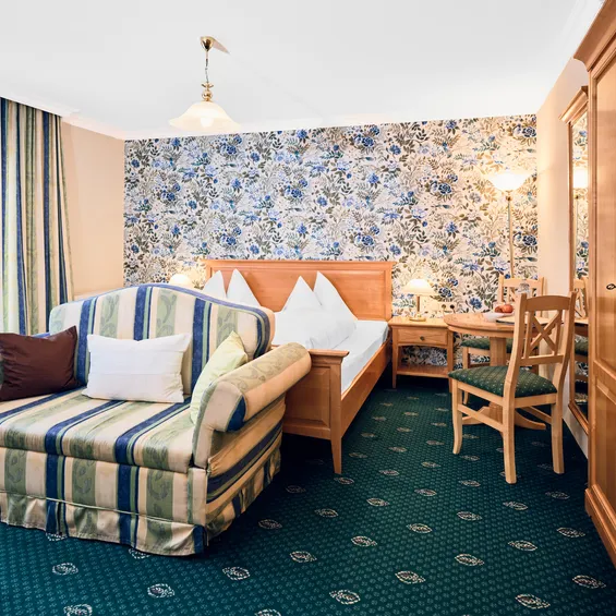Cozy hotel room with floral wallpaper, striped loveseat, wooden furniture, and double bed