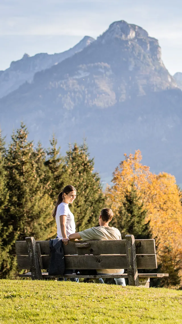 Paar auf Bank genießt Bergblick mit Herbstbäumen und See in den österreichischen Alpen