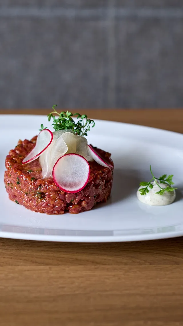 Beef tartare garnished with radish slices and herbs on a white plate