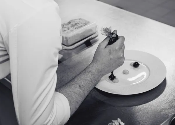 Chef decorating a plated dessert with precision in a professional kitchen