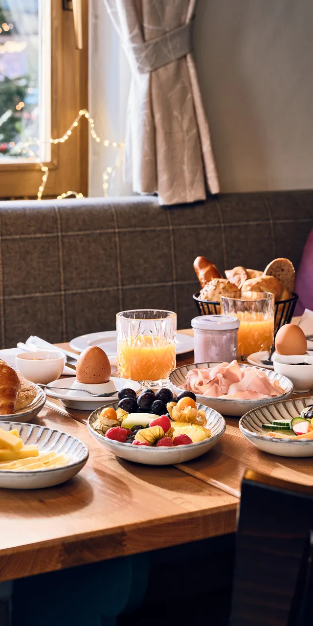 Cozy breakfast spread with croissants, juice, fruit, eggs, and coffee in a festive setting