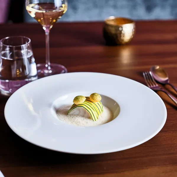 Gourmet plated dish with foam sauce, zucchini garnish, and delicate presentation on a white plate
