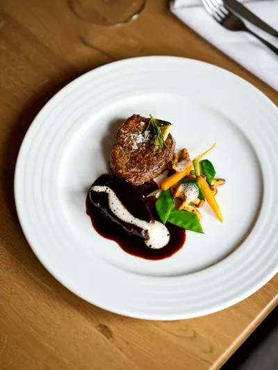 Gourmet steak with red wine sauce, baby carrots, snow peas, and mushrooms on a white plate