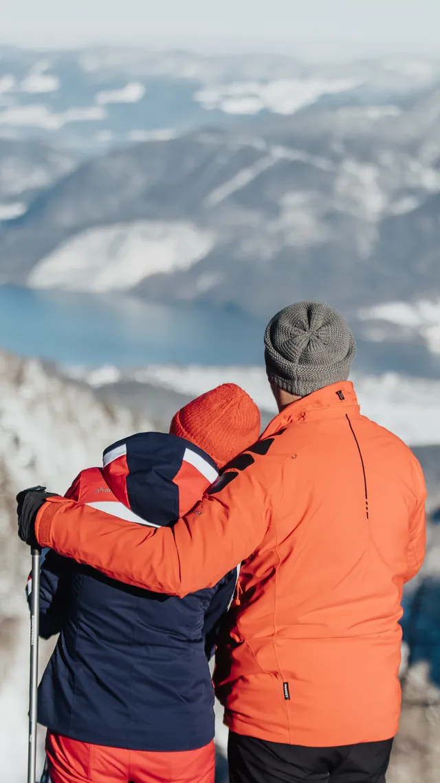 Couple in winter hiking gear admiring snowy alpine mountain landscape with lake view