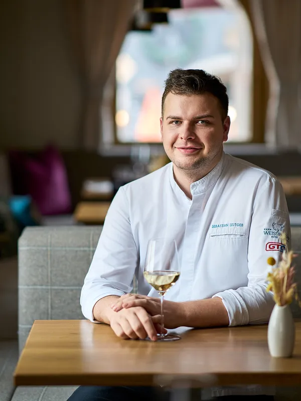 Koch in weißer Uniform sitzt am Restauranttisch mit einem Glas Weißwein