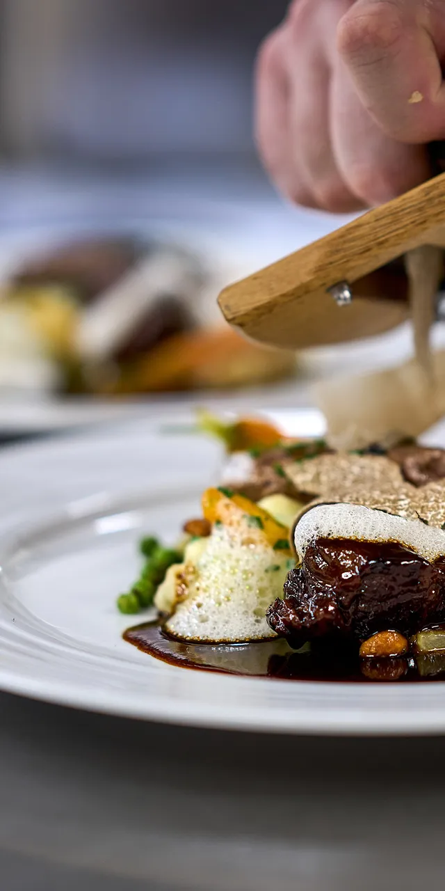 Chef grating fresh truffle over gourmet beef dish with mashed potatoes and vegetables