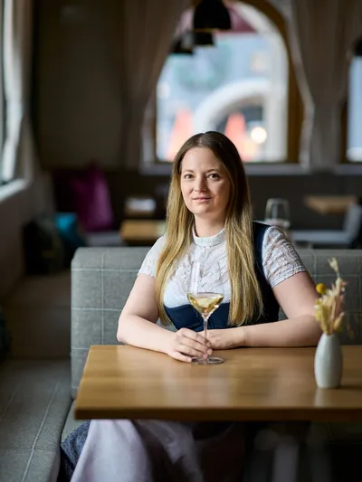 Woman with long blond hair holding a wine glass seated in a stylish restaurant interior