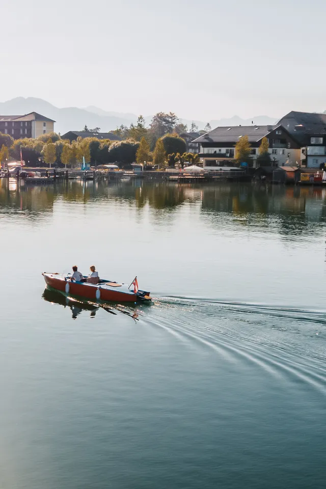 Paar in kleinem Boot auf klarem Alpensee nahe malerischem österreichischem Dorf und Bergen