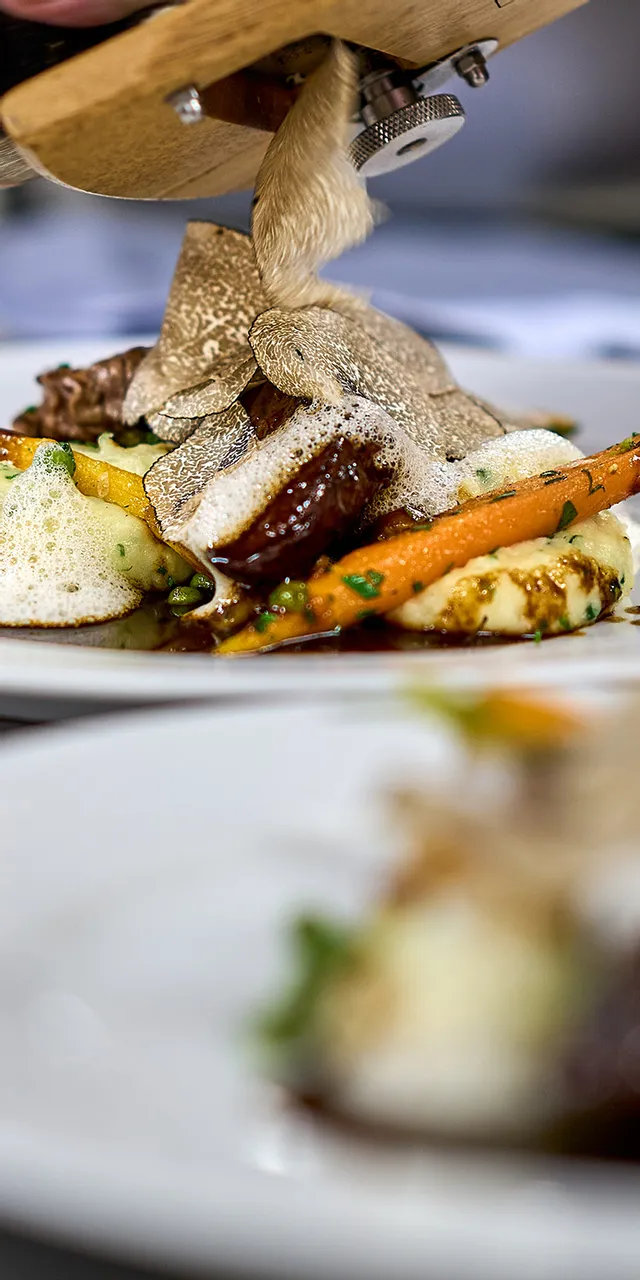 Koch hobelt frische Trüffel auf Gourmetgericht mit Fleisch, Kartoffelpüree und Karotten