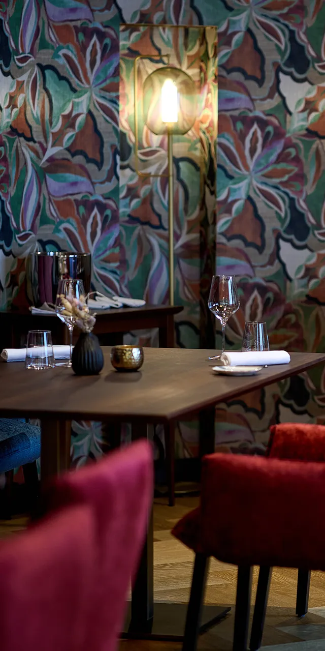 Elegant restaurant interior with velvet chairs, floral wallpaper and neatly set tables
