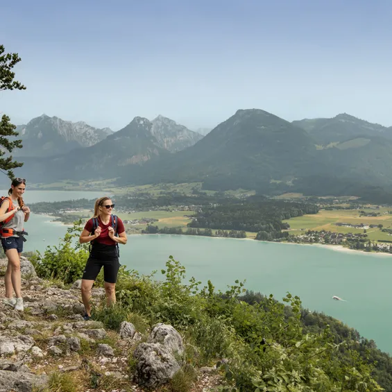 Two women hiking above turquoise lake with alpine mountain views in summer
