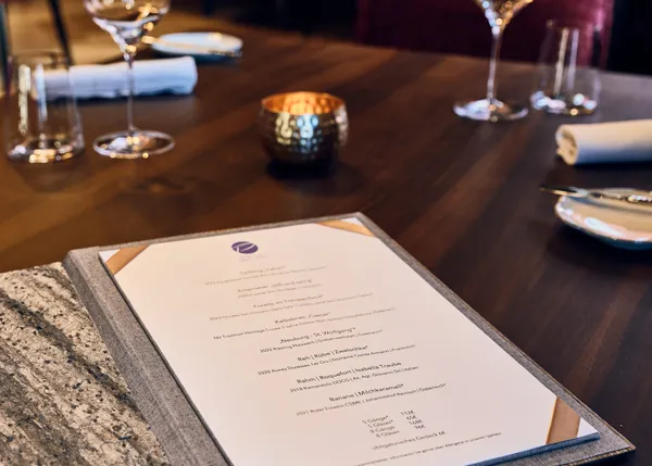 Elegant gedeckter Restauranttisch mit offener Speisekarte, Weingläsern und Kerze auf Holztisch