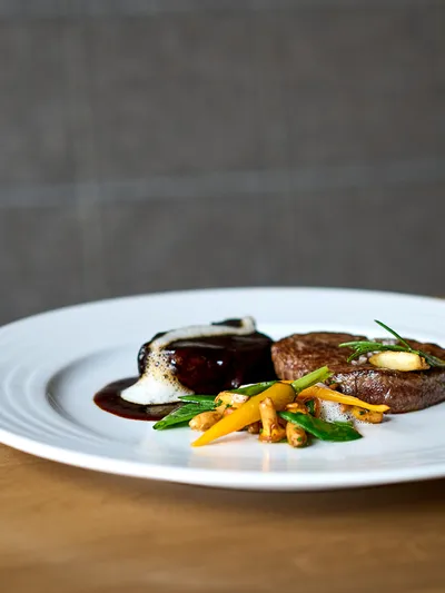 Gourmet-Rinderfilet mit Gemüse und Schaumsauce auf einem weißen Teller