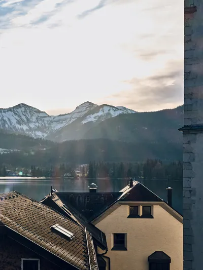 Schneebedeckte Berge und Seeblick hinter Dächern eines Alpendorfs bei Sonnenaufgang