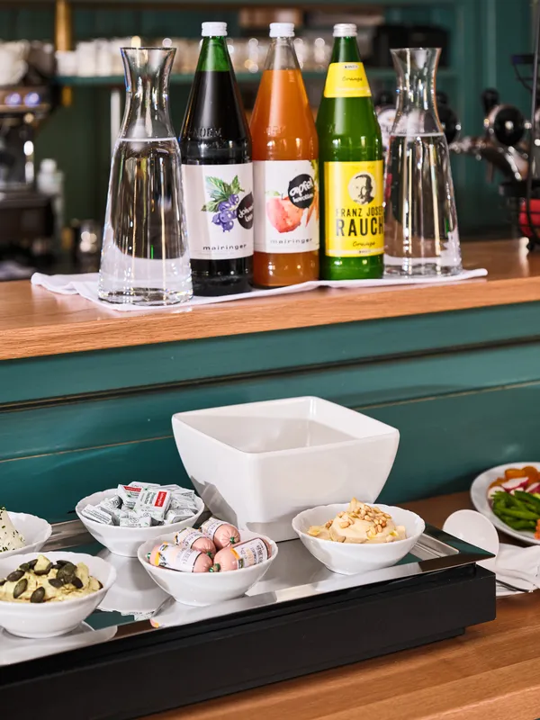 Frühstücksbuffet mit Säften, frischem Obst, Gemüse, Aufstrichen und Kaffeemaschine im Hintergrund