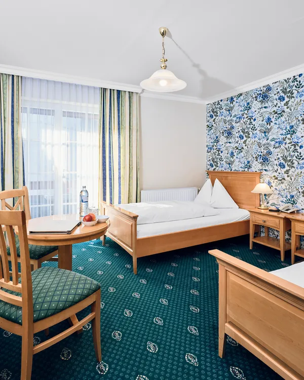 Bright hotel room with two single beds, floral wallpaper, table, chairs, and a TV