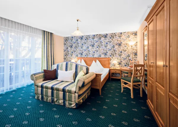 Gemütliches Hotelzimmer mit Blumenmuster-Tapete, gestreiftem Sofa, Doppelbett und Holzmöbeln
