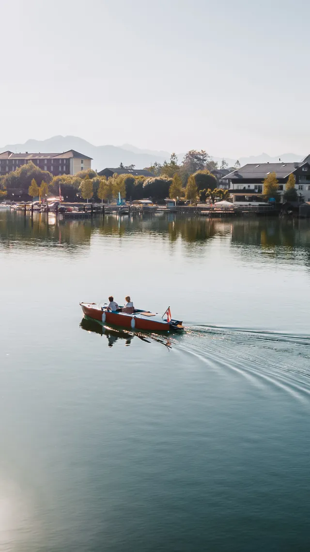 Couple in a small boat on clear alpine lake near picturesque Austrian village and mountains