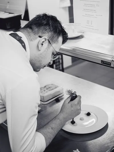 Chef decorating a plated dessert with precision in a professional kitchen